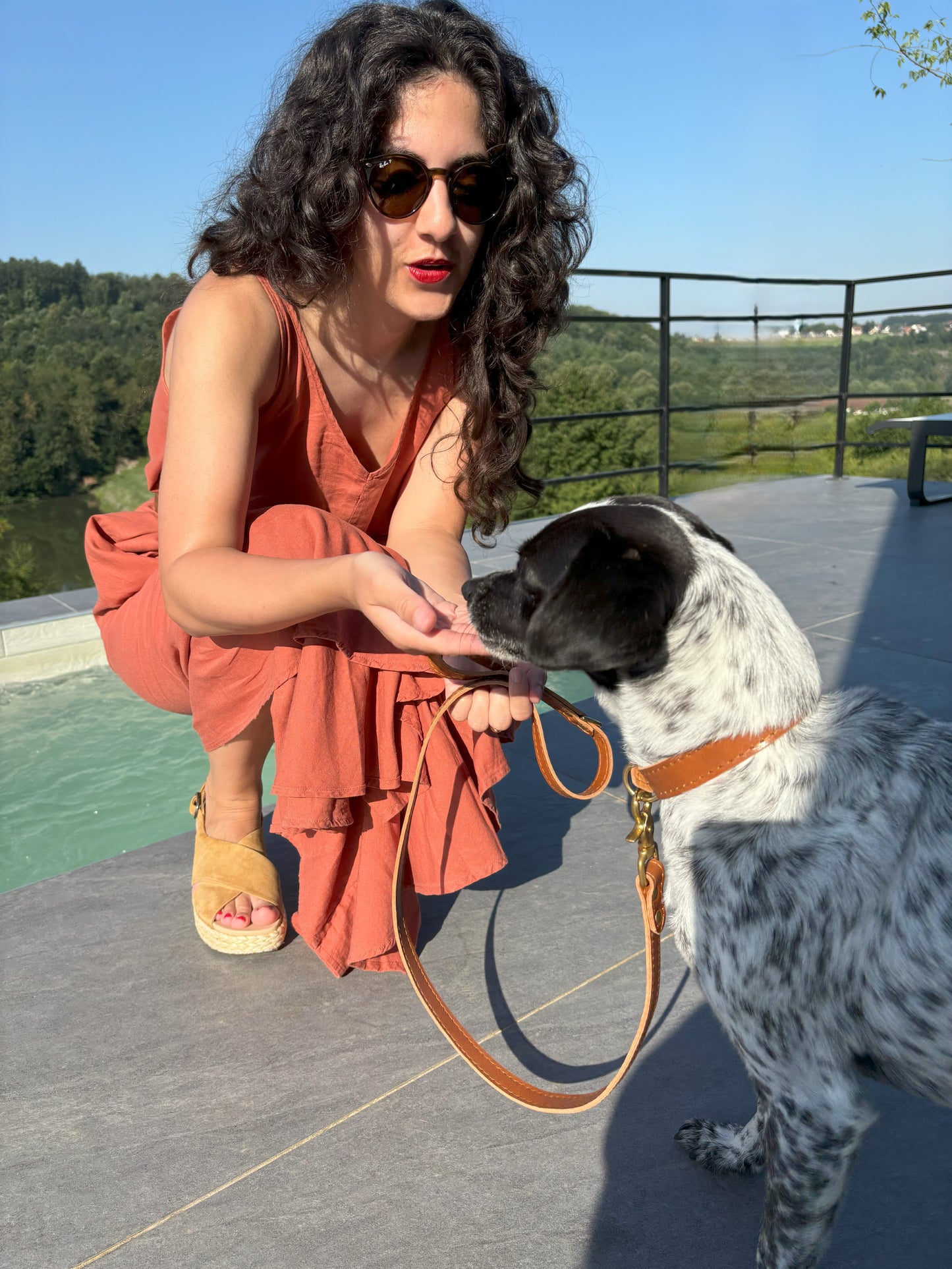 Woman giving a treat to her dog, who is wearing the matching caramel leather collar and leash set with golden brass hardware, exuding luxury and warmth.